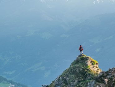 Ein Wanderer steht auf einem felsigen Berggipfel im Großarltal und blickt auf ein weites, nebliges Tal.