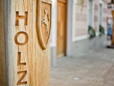 Eine hölzerne Säule mit dem Wort HOLZ und einem geschnitzten Schild mit einem Pferd auf einem städtischen Gehweg.