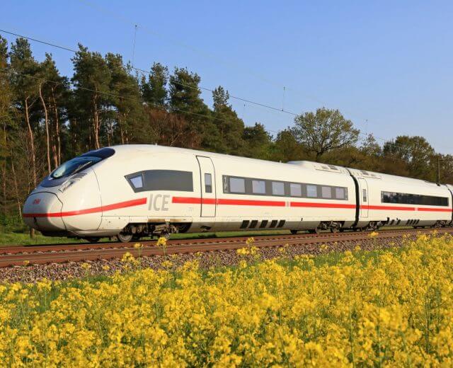 Von Paris nach Frankfurt am Main Ein weißer Hochgeschwindigkeits-ICE-Zug fährt durch eine Landschaft mit gelben Blumen und grünen Bäumen.