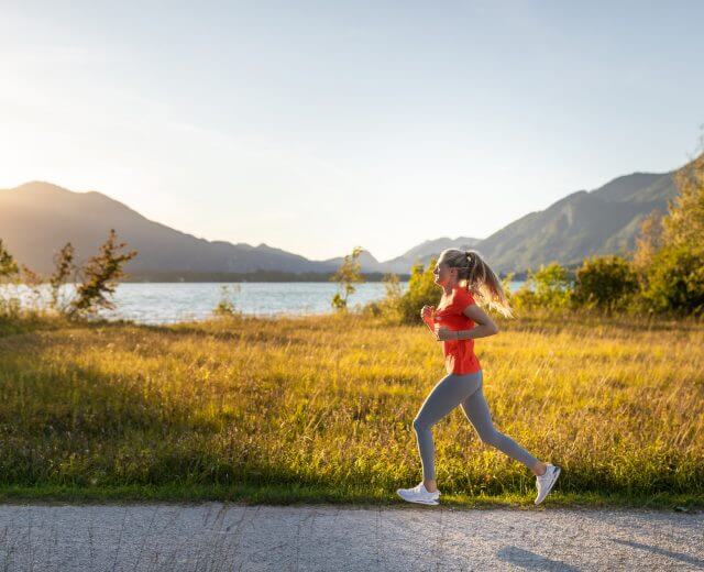 Laufen am Wolfgangsee Eine Frau joggt bei Sonnenuntergang an einem See - ein inspirierender Moment mit Bergen und Wiesen im Hintergrund.