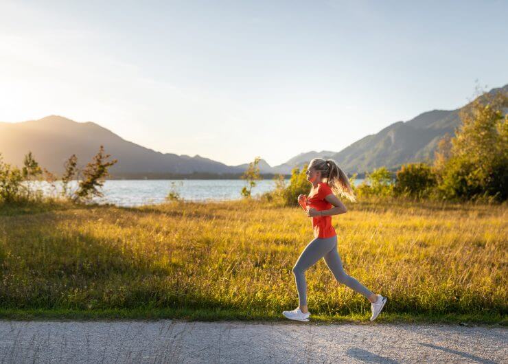 Laufen am Wolfgangsee Eine Frau joggt bei Sonnenuntergang an einem See - ein inspirierender Moment mit Bergen und Wiesen im Hintergrund.