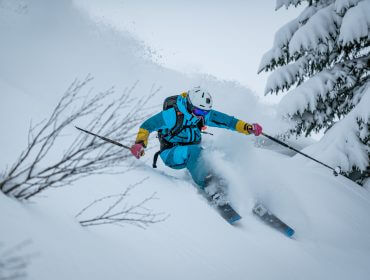 Ein Skifahrer in blauer Ausrüstung fährt eine scharfe Kurve durch den frischen Pulverschnee auf einem verschneiten Berghang.