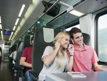 _L3C0098 Ein lächelndes junges Paar teilt sich Kopfhörer und hört Musik in einem Zug durch den malerischen Pongau.