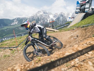 Mountainbiker fahren während der Weltmeisterschaften auf einer unbefestigten Strecke bergab, mit Bergen im Hintergrund.