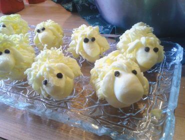 Desserts in Schafsform mit weißer Glasur und Schokoladenaugen auf einem Glastablett.
