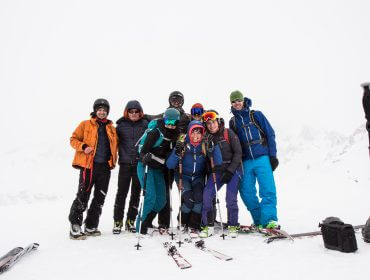 Eine Gruppe von acht Personen in Skikleidung posiert gemeinsam auf dem verschneiten Schöpfling mit Skistöcken und Skiern.