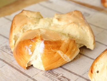 Ein goldglänzendes, gebackenes Brötchen mit gespaltener Oberseite, das auf Backpapier liegt.