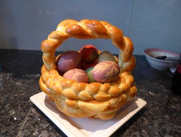 Ein geflochtener Brotkorb, gefüllt mit verzierten Ostereiern, steht auf einem weißen Teller auf einer dunklen Arbeitsplatte.