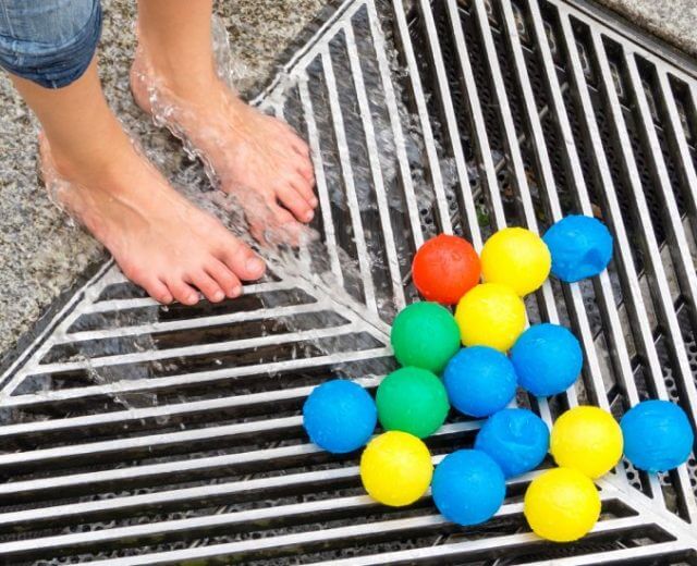 Stadt für Kinder Nackte Füße auf einem nassen Metallgitter neben bunten Plastikbällen - gelb, blau, grün und rot.