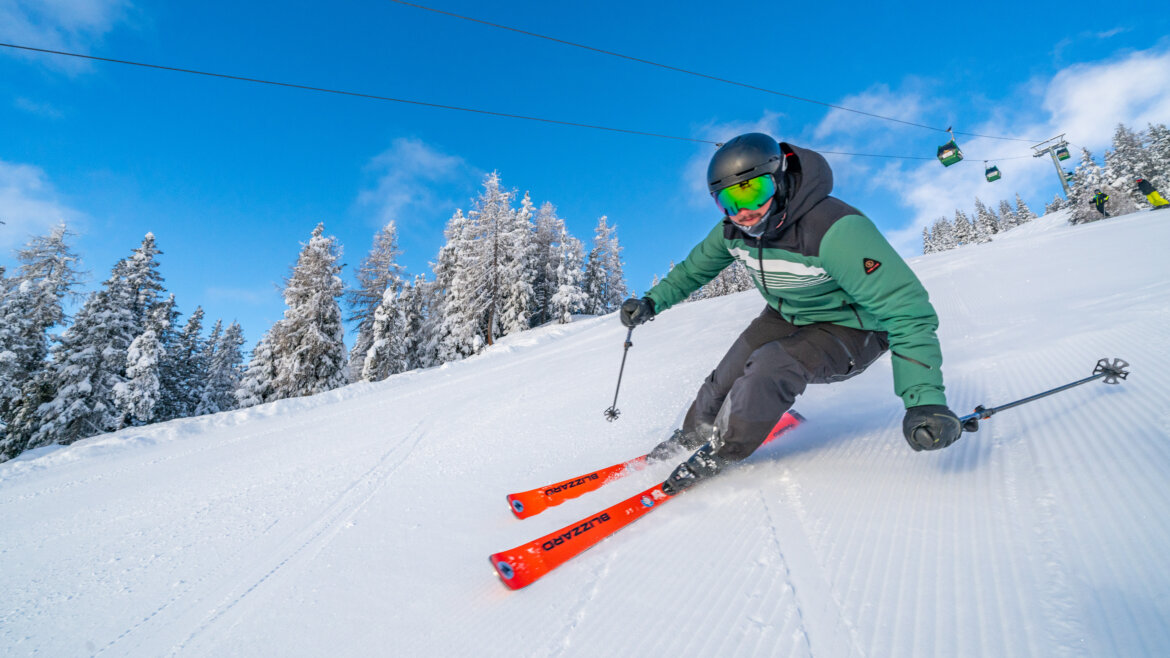 Peter Maier, Peter Maier Ein Skifahrer in grüner und schwarzer Ausrüstung fährt an einem sonnigen Tag einen verschneiten Wildkogelhang hinunter, mit Bäumen im Hintergrund. (vergrößerte Ansicht)