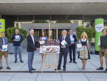 Eine Gruppe von Menschen posiert mit Broschüren vor dem Ferry Porsche Congress Center und einer Lebensmittelausstellung auf einer Staffelei.