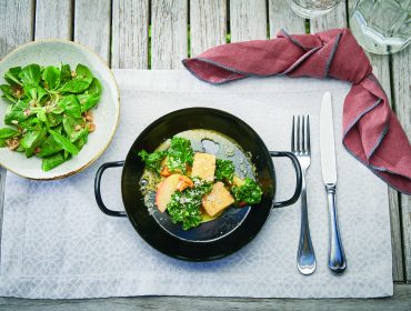 Ein Salat und ein Hauptgericht mit Gemüse und Käse werden auf einem Tisch mit Gabel, Messer und roter Serviette angerichtet.