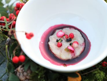 Eine weiße Schale mit einem Gourmet-Teller mit einer runden Portion in lila Sauce, garniert mit rosa Blumen.