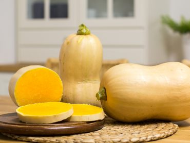 Rezepte-mit-Kurbis Drei Butternusskürbisse, ein ganzer, ein halbierter und zwei in Scheiben geschnittene, auf einem Tisch in einer Küche.