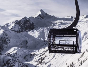 Explorer_tour_kabine Eine Skigondel mit der Bezeichnung "Explorer" gleitet an einem klaren Wintertag über die verschneiten Alpengipfel des Kitzsteinhorns.