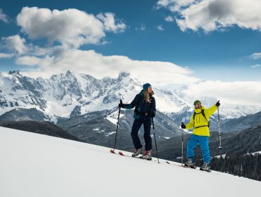 Pärchen auf Skitour Zwei Personen fahren auf einem verschneiten Berghang mit schneebedeckten Gipfeln im Hintergrund bergauf.