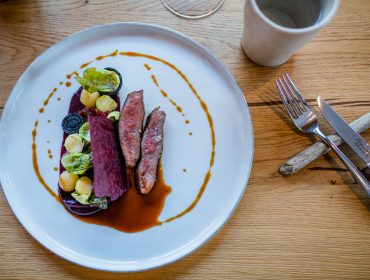 SLT_Zillner_-(100-of-110) Ein Gourmet-Teller von Florian Zillner mit geschnittenem Fleisch, Gemüse und Soße auf einem weißen Teller neben einer Tasse.