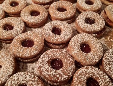 Mit Puderzucker bestäubte, runde Sandwich-Kekse mit Marmeladenkern, die dicht aneinandergereiht sind.