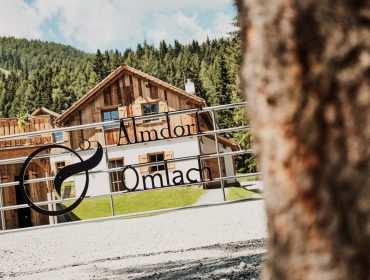 Eine rustikale Holzhütte im Almdorf Omlach, eingebettet zwischen Bäumen und Bergen.