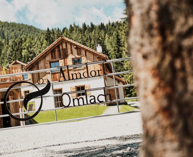 _®KWER_Almdorf-Omlach-(8) Eine rustikale Holzhütte im Almdorf Omlach, eingebettet zwischen Bäumen und Bergen.