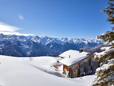 Eine verschneite Berghütte im Nationalpark Hohe Tauern mit schneebedeckten Bäumen und fernen Gipfeln unter einem klaren blauen Himmel.