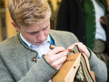 Federkiel Stickerei, Bauernherbst, Handwerk Ein junger Mann näht sorgfältig mit Nadel und Faden ein detailliertes Muster auf den Stoff.