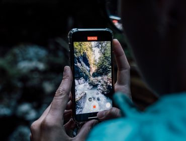 Saalachtal Seisenbergklamm Person, die ein Telefon hält und eine Naturszene mit einem felsigen Bach und Bäumen auf dem Bildschirm aufnimmt.