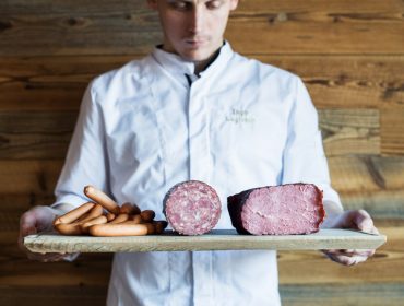 Ein Koch hält ein Holzbrett mit Würsten, Salami und gepökeltem Fleisch für puren Genuss.