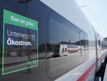 Ein moderner deutscher Zug in einem Bahnhof mit einem Schild über umweltfreundlichen Ökostrom und nachhaltige Mobilität.