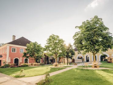Charmante Gebäude mit gewölbten Gängen und Sitzgelegenheiten im Freien, die mit Nachhaltigkeit inmitten von grünen Rasenflächen und Bäumen gestaltet wurden.