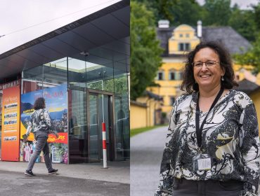 0J3A4933 Eine Frau in einer gemusterten Bluse betritt ein Gebäude und lächelt, während sie auf einem Weg mit gelben Gebäuden steht.