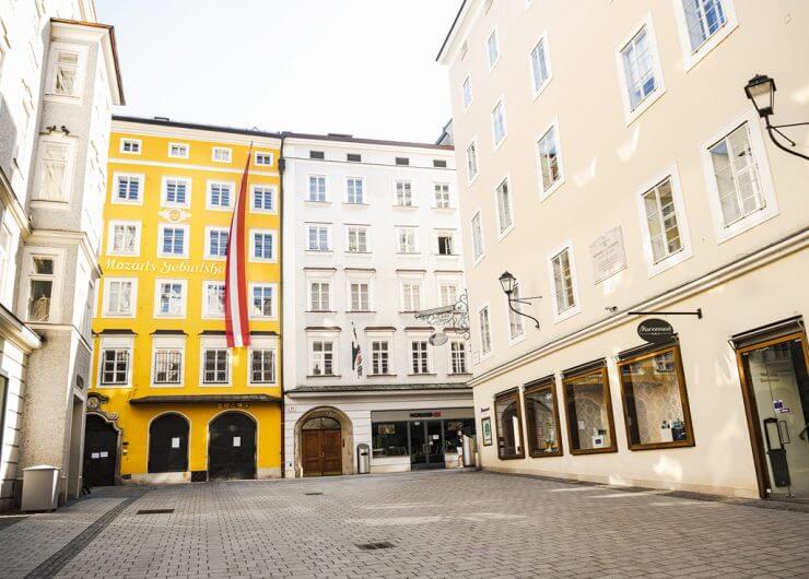 Ein sonniger, leerer Platz mit Kopfsteinpflaster und Mozarts Geburtshaus, ein gelbes Gebäude, in Salzburg, Österreich.