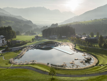 Der große, malerische Außenpool des Krallerhofs mit Sonnenschirmen und Liegen liegt in einem üppigen Tal inmitten nebliger Berge.