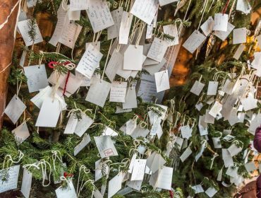 Ein Weihnachtsbaum mit handgeschriebenen Zetteln und Karten, die mit Schnüren an den Zweigen befestigt sind.