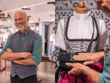 Lächelnder Mann in einem Geschäft, der mit seinen Händen ein österreichisches Trachtenkleid an einer Schaufensterpuppe zurechtrückt.