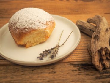 Mit Puderzucker bestreutes Gebäck auf einem weißen Teller mit Lavendelzweigen und Treibholz auf einem Holztisch.