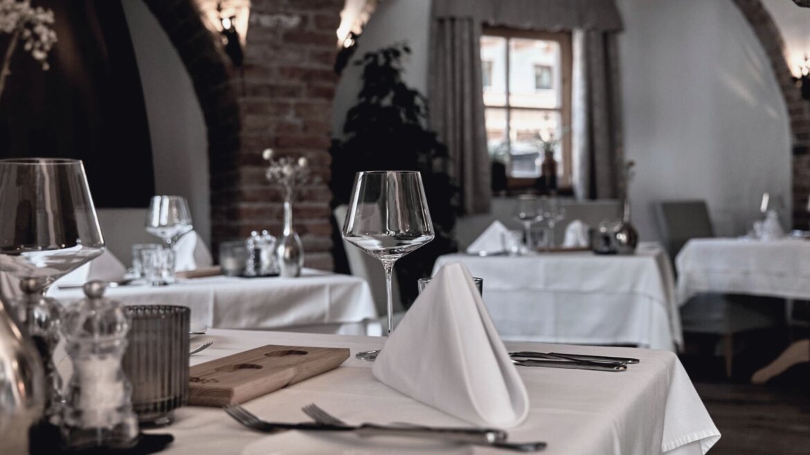 Elegantes Restaurant mit weißen Tischtüchern und gewölbten Ziegelwänden in der Hochkönigin, sanft beleuchtet von natürlichem Licht. (vergrößerte Ansicht)