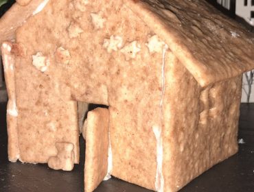 Ein selbstgebackenes Lebkuchenhaus mit einer leicht geöffneten Tür, verziert mit weißem Zuckerguss und Sternenmustern.