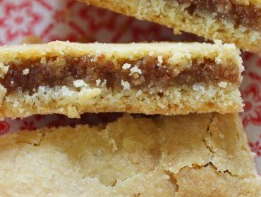 Drei Stücke Mürbegebäck mit brauner Füllung auf einem rot-weiß gemusterten Tuch.