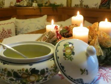 Eine Suppenterrine mit Löffel auf einem Tisch mit vier brennenden Kerzen und festlicher Dekoration in einem gemütlichen Raum.