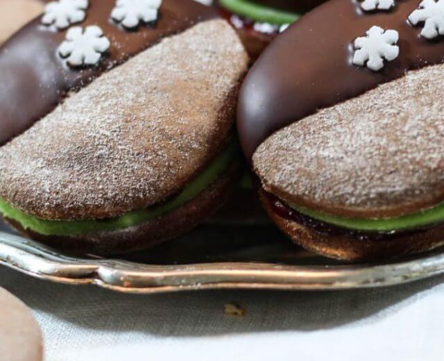 In Schokolade getauchte Kekse mit weißer Schneeflockenverzierung, gefüllt mit grüner Creme, auf einem silbernen Tablett.