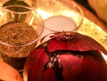 Nahaufnahme einer roten Zwiebel, einer gelben Zwiebel, von schwarzem Pfeffer und Salz in Schalen auf einem goldenen Tablett.