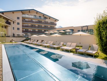 Außenpool mit Liegestühlen im Hotel Mavida Haidvogl, an einem sonnigen Tag im Schatten der Sonnenschirme.