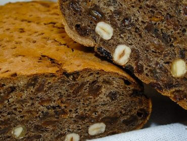 Eine Nahaufnahme eines dunklen, nussbestückten Brotes, das in zwei Hälften geschnitten wurde, zeigt seine dichte Textur und sein reichhaltiges, rustikales Aussehen.