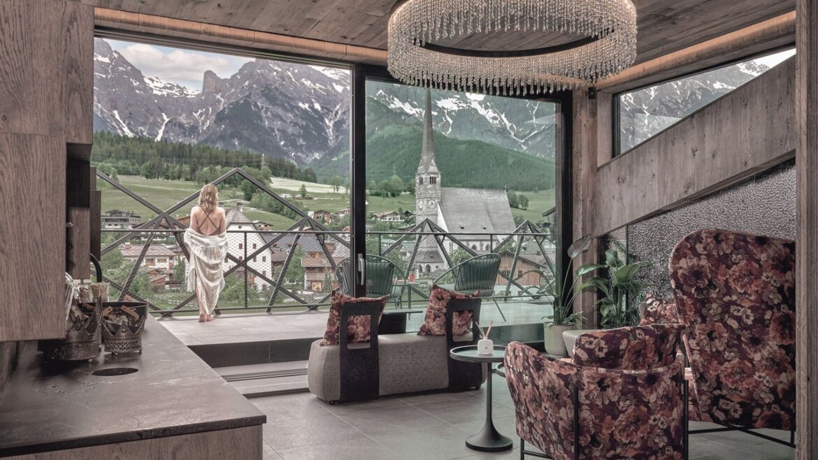 Frau im Handtuch auf einem Balkon der Hochkönigin mit Blick auf ein Alpendorf und die Berge. (vergrößerte Ansicht)