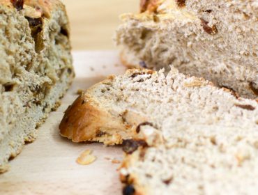 Nahaufnahme eines in Scheiben geschnittenen Rosinenbrots mit Haferflocken auf einem Holzschneidebrett.