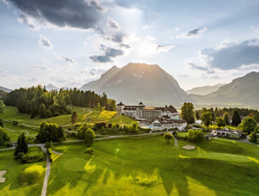 Eine Hotelanlage in der Nähe des Golfclubs Schloss Pichlarn, umgeben von grünen Hügeln und Bergen bei Sonnenuntergang.