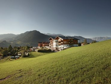 Gebäude des Hotels Sonnhof auf einem grasbewachsenen Hügel mit Bergen und klarem Himmel im Hintergrund.