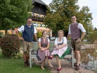 Vier Personen in traditioneller österreichischer Kleidung posieren auf einer Bank in der Gartenanlage des Gastagwirts.