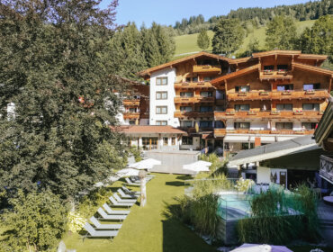 Das Hotel Sonne ist ein Berghotel mit Holzbalkonen, Liegestühlen, Sonnenschirmen und einem Pool in einem grünen Garten.
